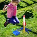 Child jumping in excitement by an air-powered rocket launcher in a grassy yard, ready for outdoor fun.