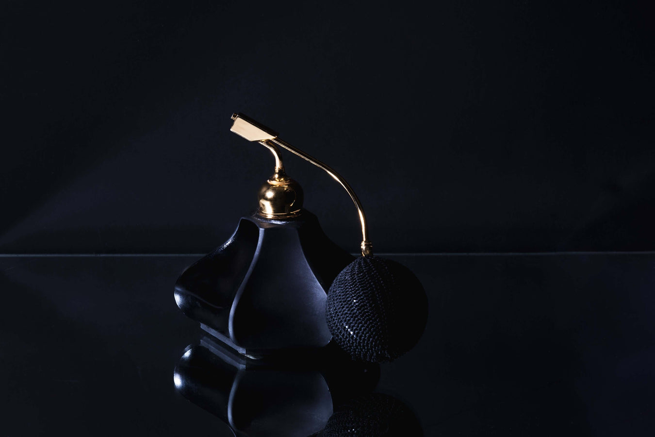 elegant black perfume bottle with a golden spray nozzle and a textured black puff, set against a dark background